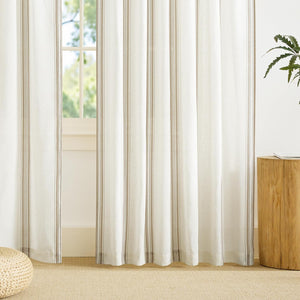 Natural cream linen-look curtain panels with subtle vertical taupe stripes cover a sunlit window.