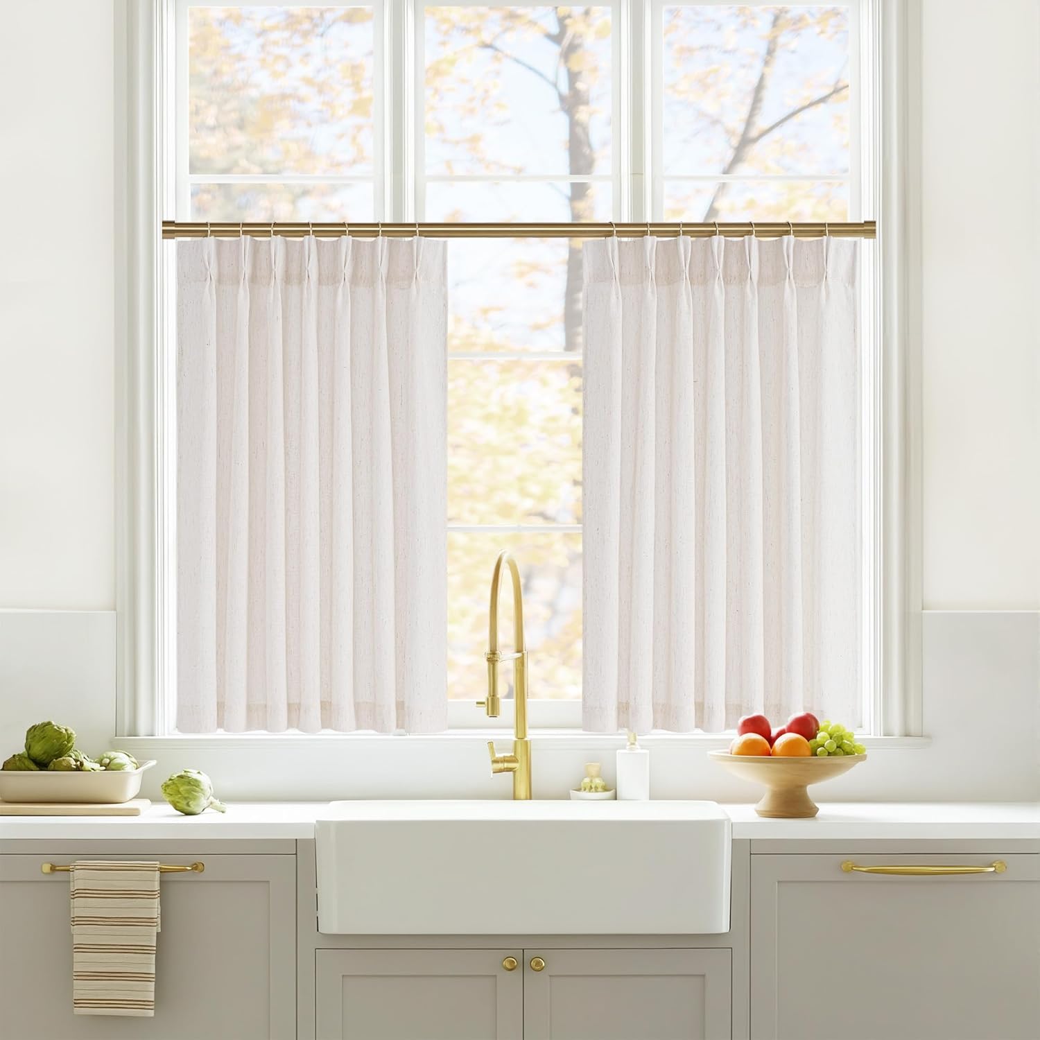 Natural linen blend pleated cafe curtains on a gold rod above a modern kitchen sink.