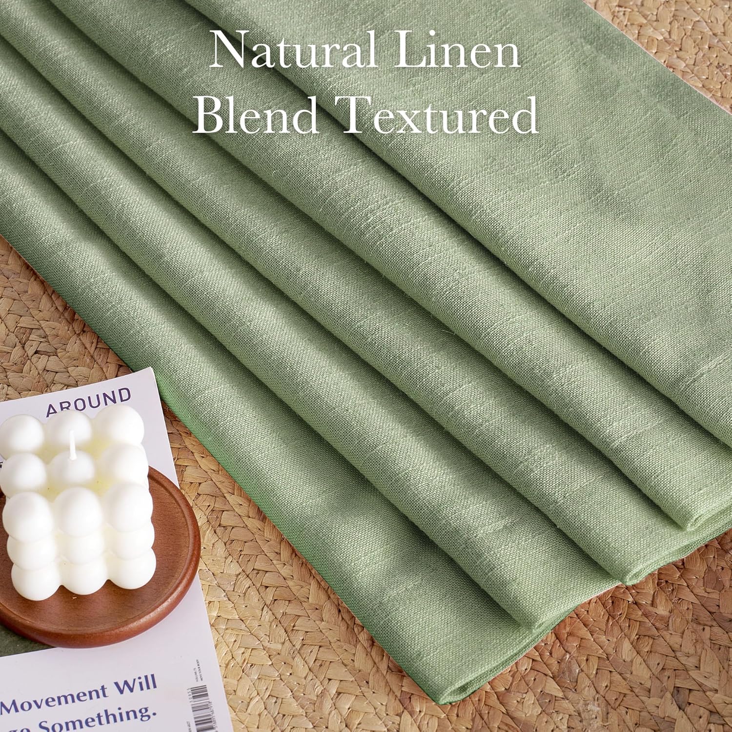 Textured sage green natural linen blend fabric folded neatly on a woven mat, next to a white bubble candle.