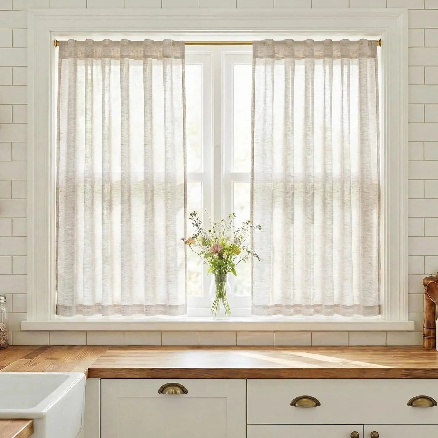 Light beige sheer linen-look cafe curtains on a brass rod in a sunny farmhouse kitchen window.