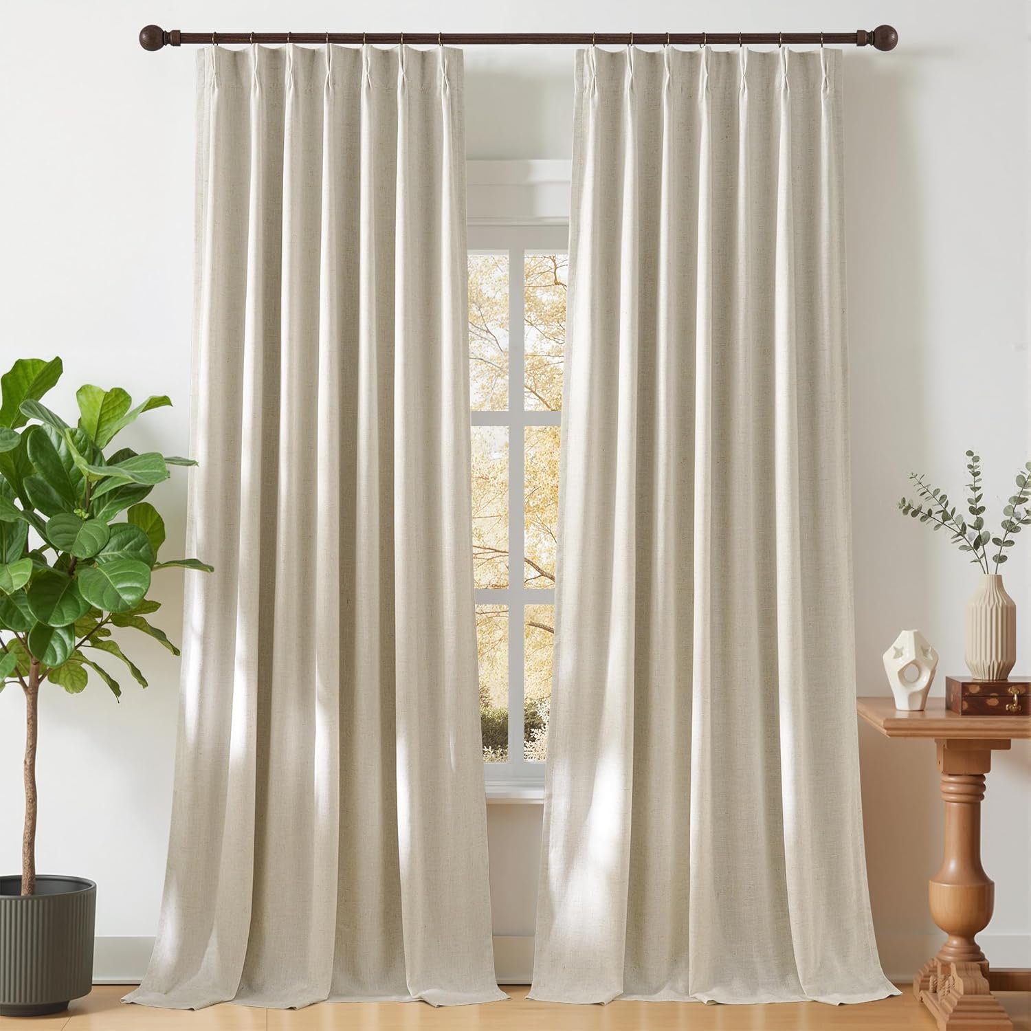Natural beige linen pinch pleat curtains hung on a dark wood rod, framing a sunny window.