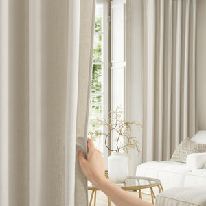 Light beige textured linen curtains with elegant pleats, pulled open by a hand, in a modern living room.
