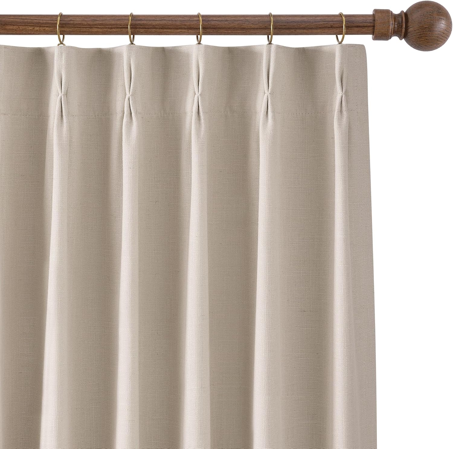 Beige linen pinch pleat drapes hanging from a dark wood curtain rod with brass rings. Visible fabric texture.