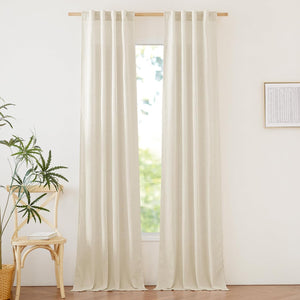 Two panels of light beige linen-look tab top curtains hanging on a wooden rod in a sunlit room.