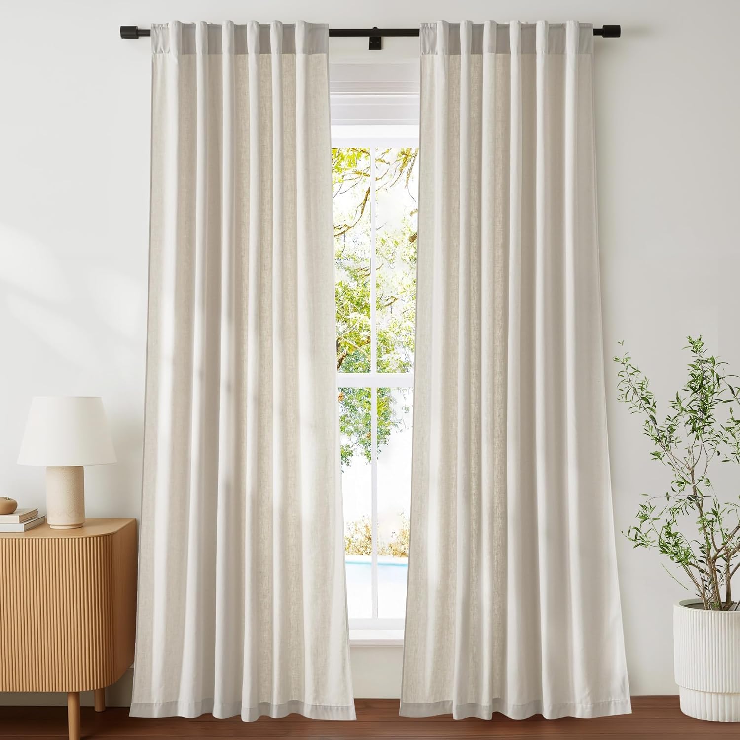 Pair of natural linen tab top light filtering curtains in a soft beige hue, hanging from a black rod.