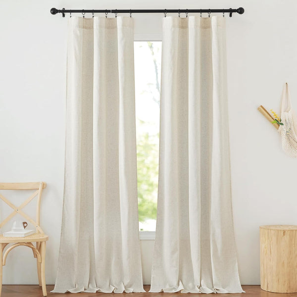 Light beige linen-textured semi-sheer curtains hang on a black rod, softly pooling on a wooden floor.