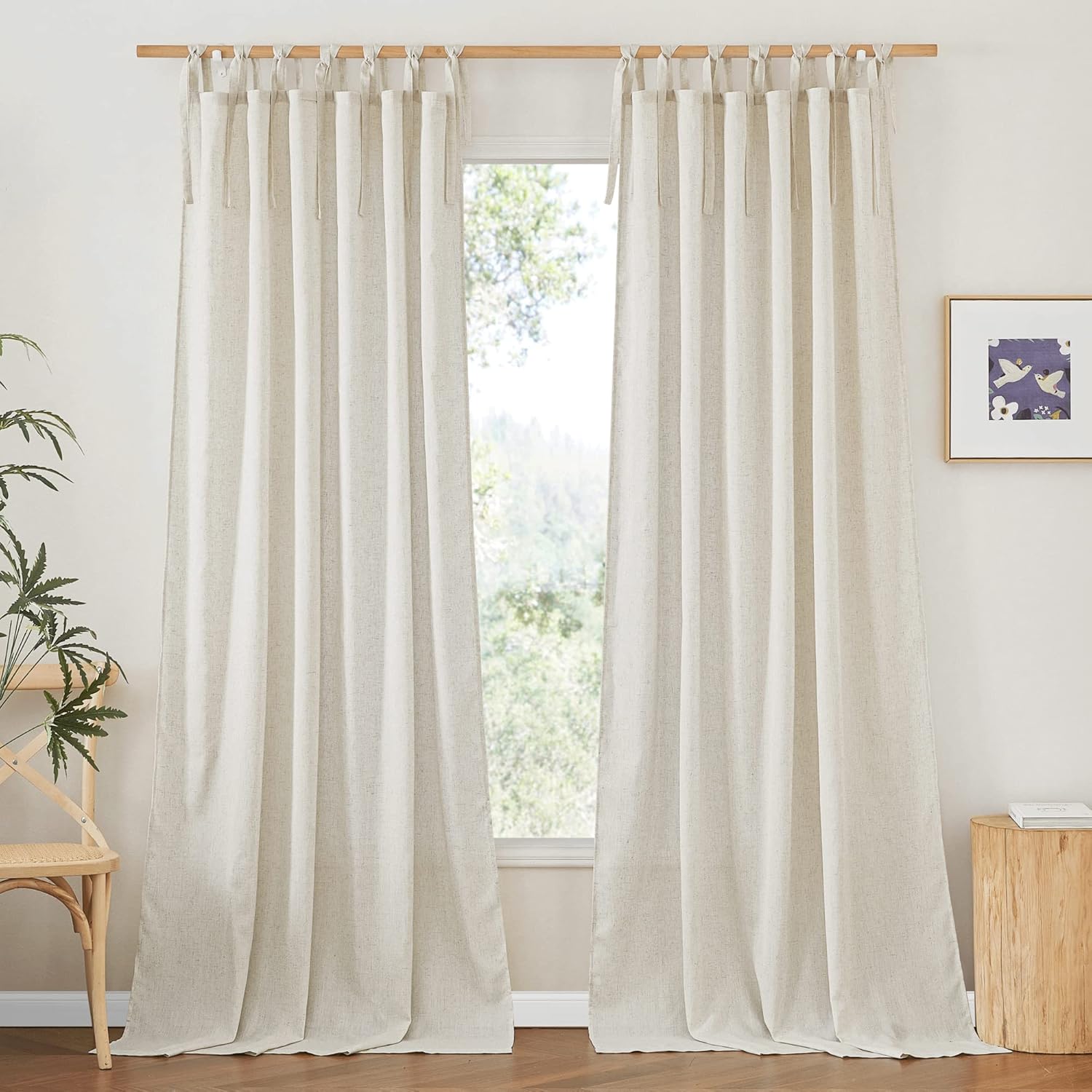 Pair of natural linen tie-top curtains with visible textured weave, hanging on a wooden rod in a sunlit room.