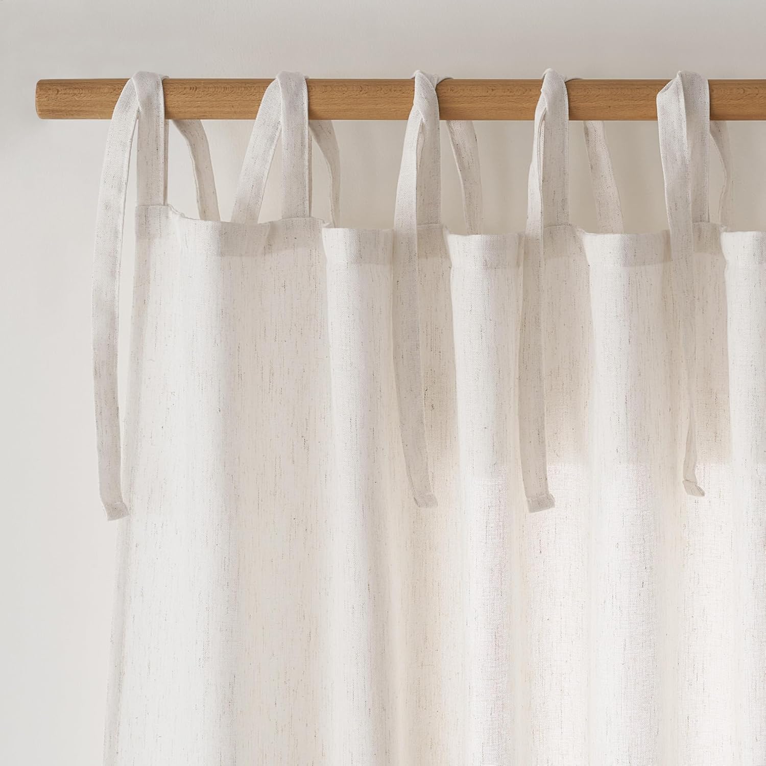 Natural off-white linen tie-top curtains with subtle texture, draped over a light wood curtain rod.
