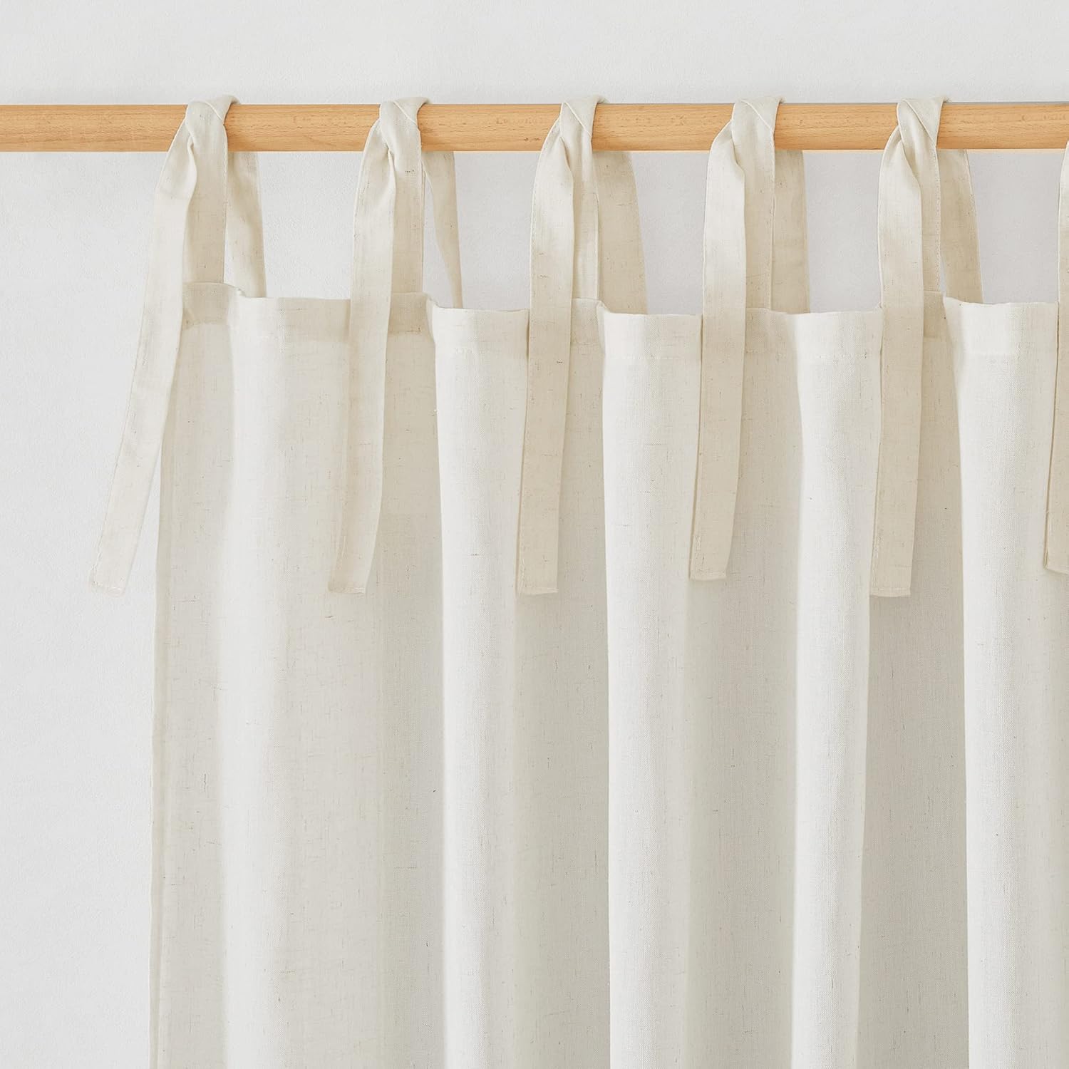 Off-white natural linen tie-top curtains with visible texture hanging from a light wood rod.