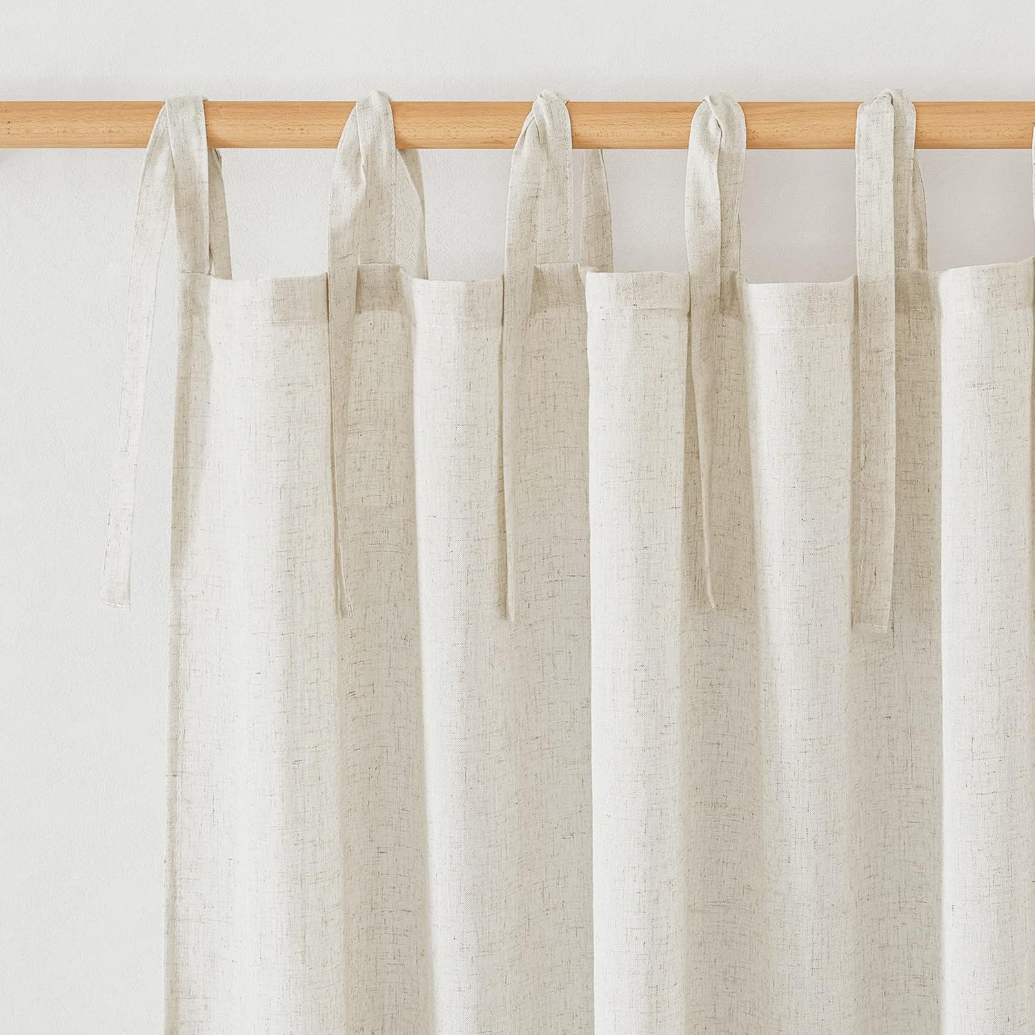 Light beige textured linen curtains with decorative tie-top loops hanging from a wooden curtain rod.