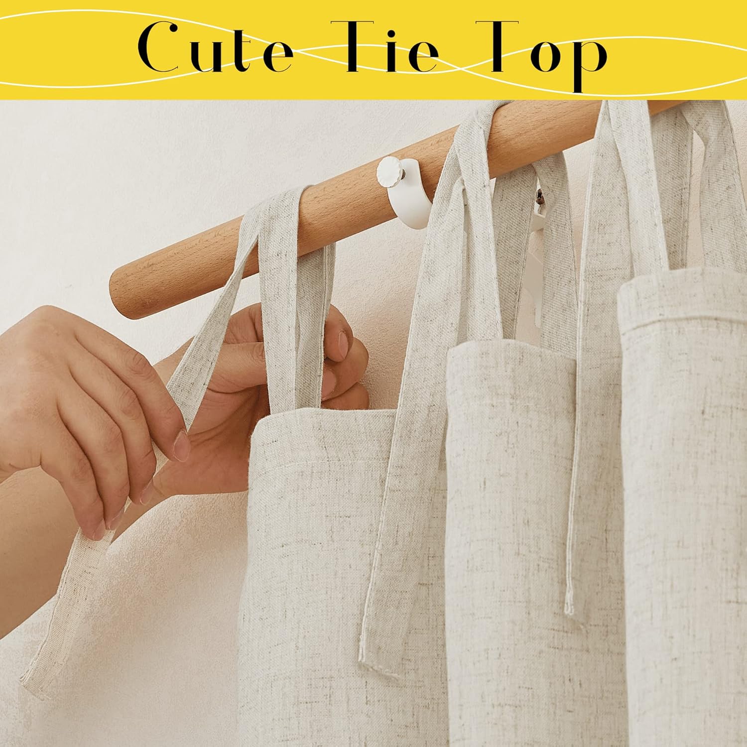 Close-up of natural linen tie-top curtains hanging on a wooden rod, with a hand tying one of the fabric straps.