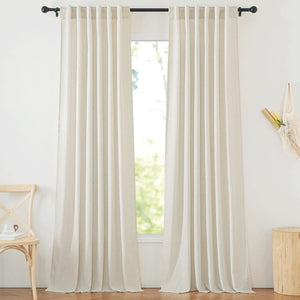 Pair of natural off-white linen-blend back tab curtains hanging on a black rod, pooling slightly on the floor.