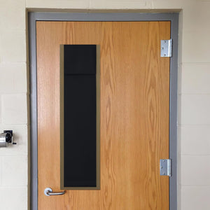 Natural wood door with grey metal frame, long black privacy window panel, chrome handle, on concrete block wall.