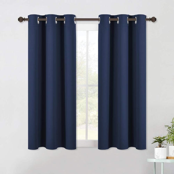 Two navy blue blackout curtains with silver grommet tops hanging from a dark bronze rod over a window.