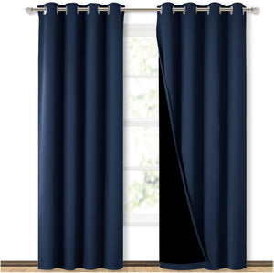 Pair of navy blue blackout curtains with silver grommets. One panel shows black lining, hanging on a window.