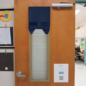 Navy blue bow-tie door window cover on a wooden classroom door, providing privacy.
