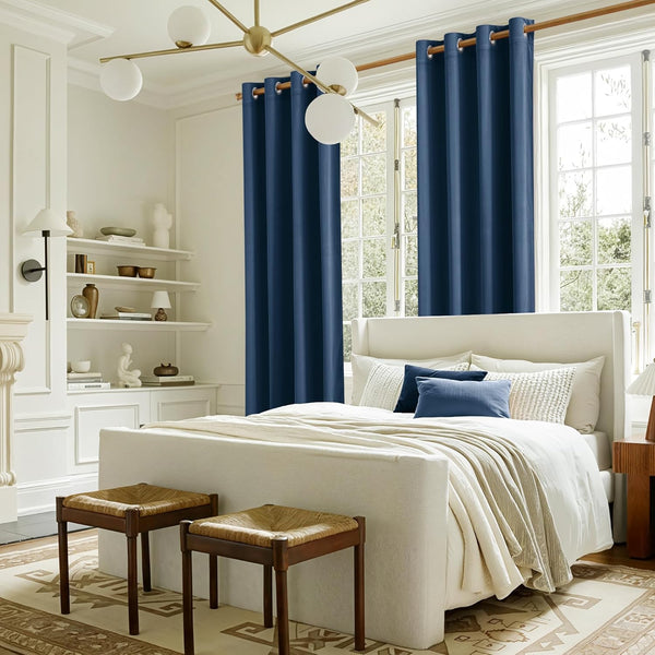 Deep navy blue grommet top blackout curtains hanging on a wooden rod in a bright, modern bedroom.