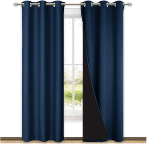 Two navy blue blackout curtains with silver grommets hang on a rod, one revealing dark lining.