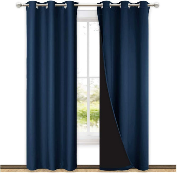 Two navy blue blackout curtains with silver grommets hang on a rod, one revealing dark lining.