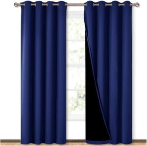 A pair of navy blue blackout curtains with grommet tops hanging on a silver rod in front of a window.