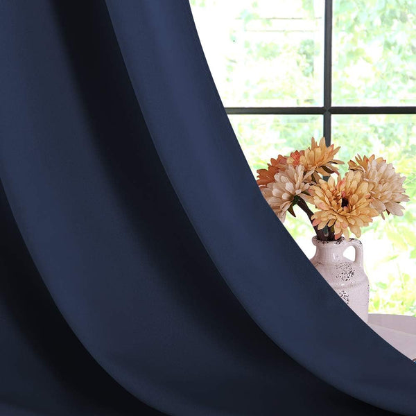 Navy blue matte blackout curtain hanging with soft folds, partly obscuring a window with flowers.