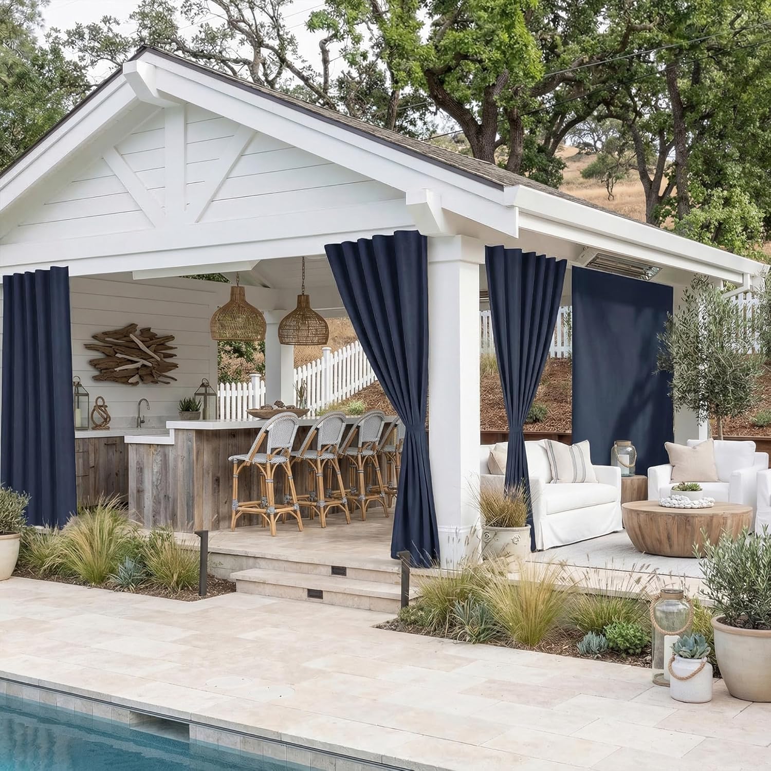Navy blue outdoor curtains on a white cabana, offering privacy for a bar and lounge by a pool.