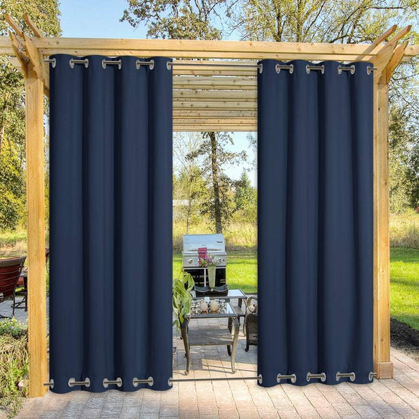 Two dark blue outdoor grommet curtains hanging from a wooden pergola, providing shade for a patio.