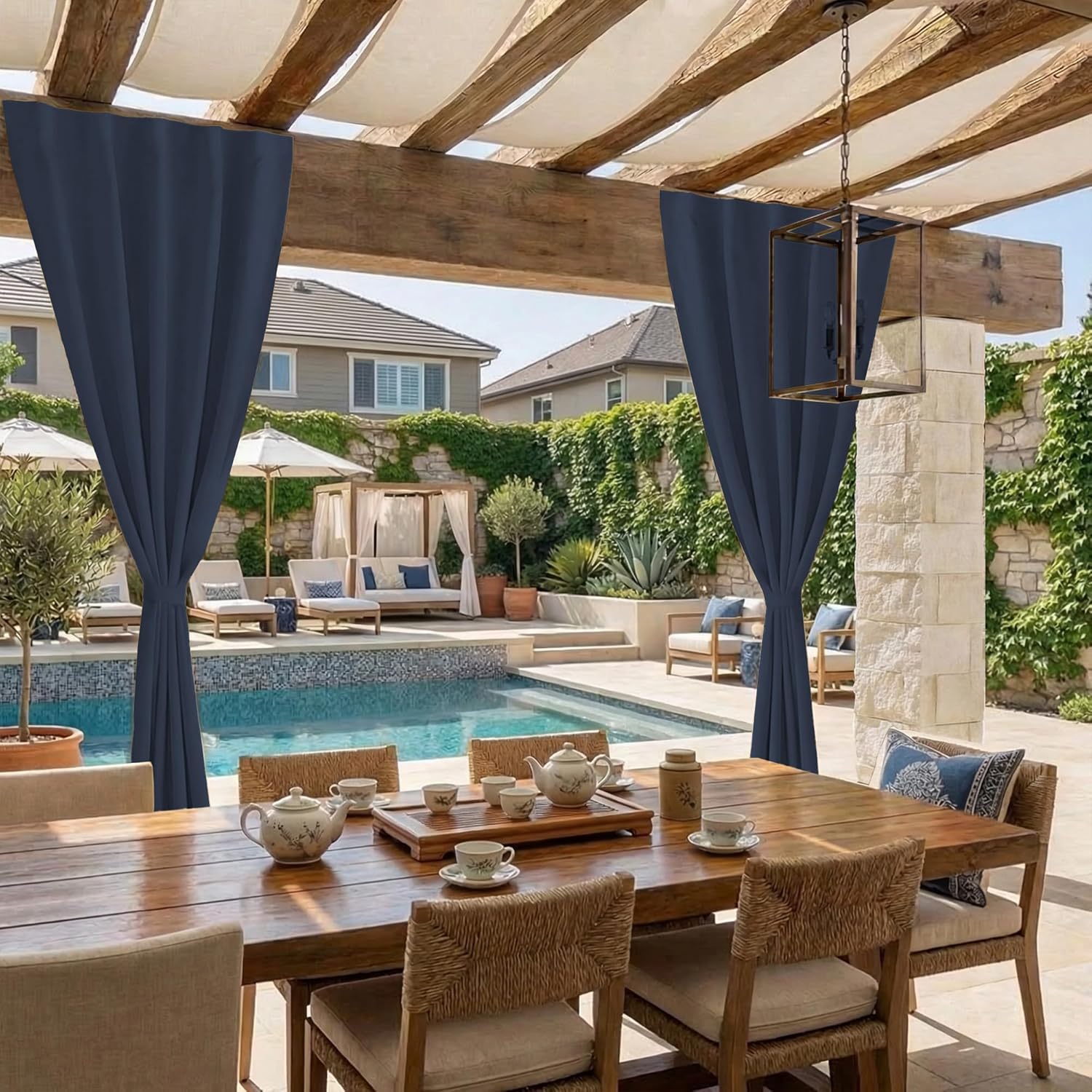 Navy blue outdoor curtains tied back on a wooden pergola, shading a patio dining table by a pool.