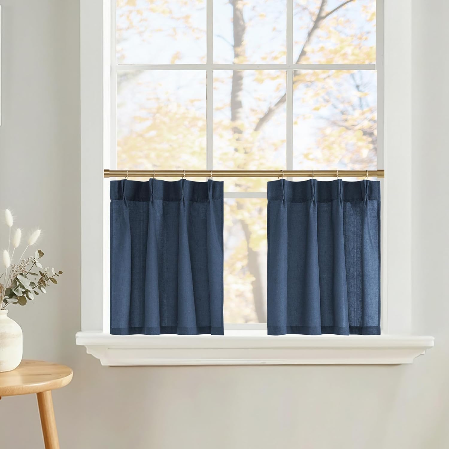 Navy blue pleated cafe curtains made of linen blend fabric, hung on a brass rod over a sunlit window.