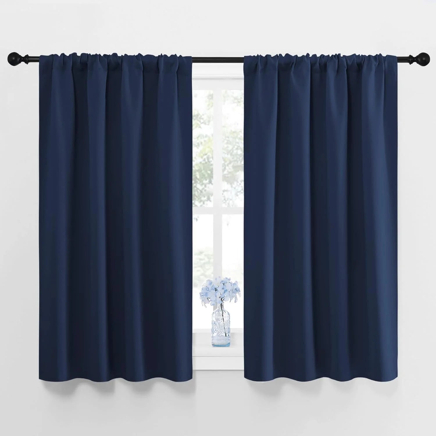 Navy blue rod pocket blackout curtains on black rod over window, with vase.