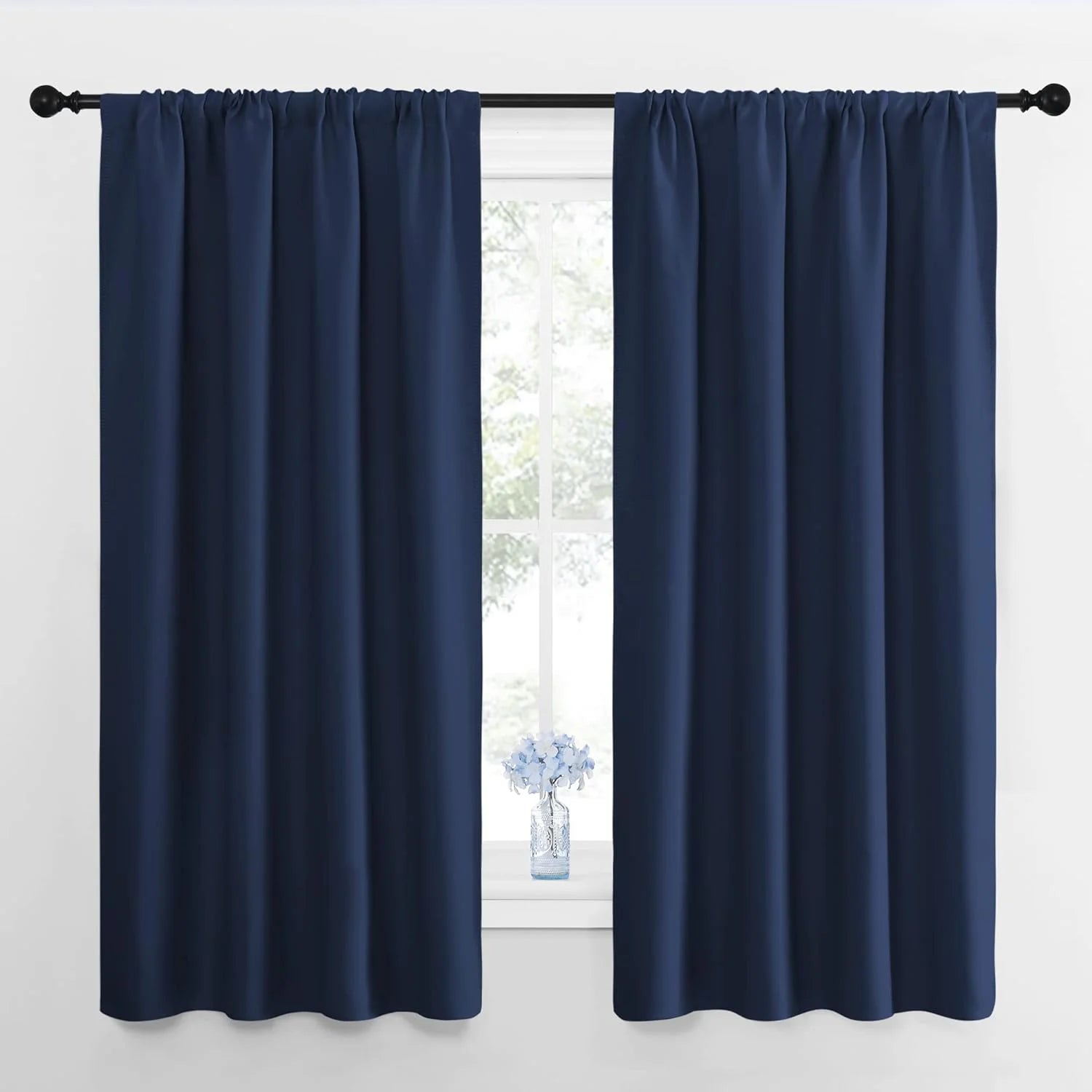 Two navy blue blackout rod pocket curtain panels on a black rod covering a window.