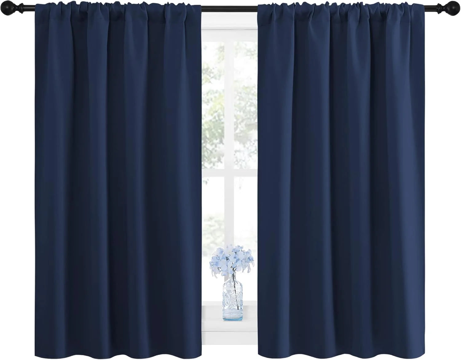 Pair of navy blue rod pocket curtains on a black rod, framing a bright window with a small vase of blue flowers.