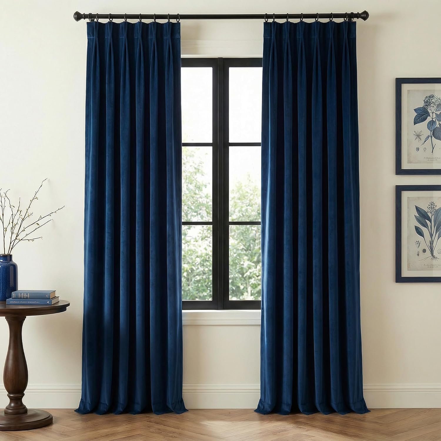 Pair of navy blue velvet pinch pleat curtains hanging on a black rod, pooling on the floor.