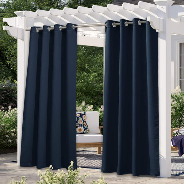 Navy blue weatherproof outdoor curtains with silver grommets hanging from a white pergola on a sunny patio.