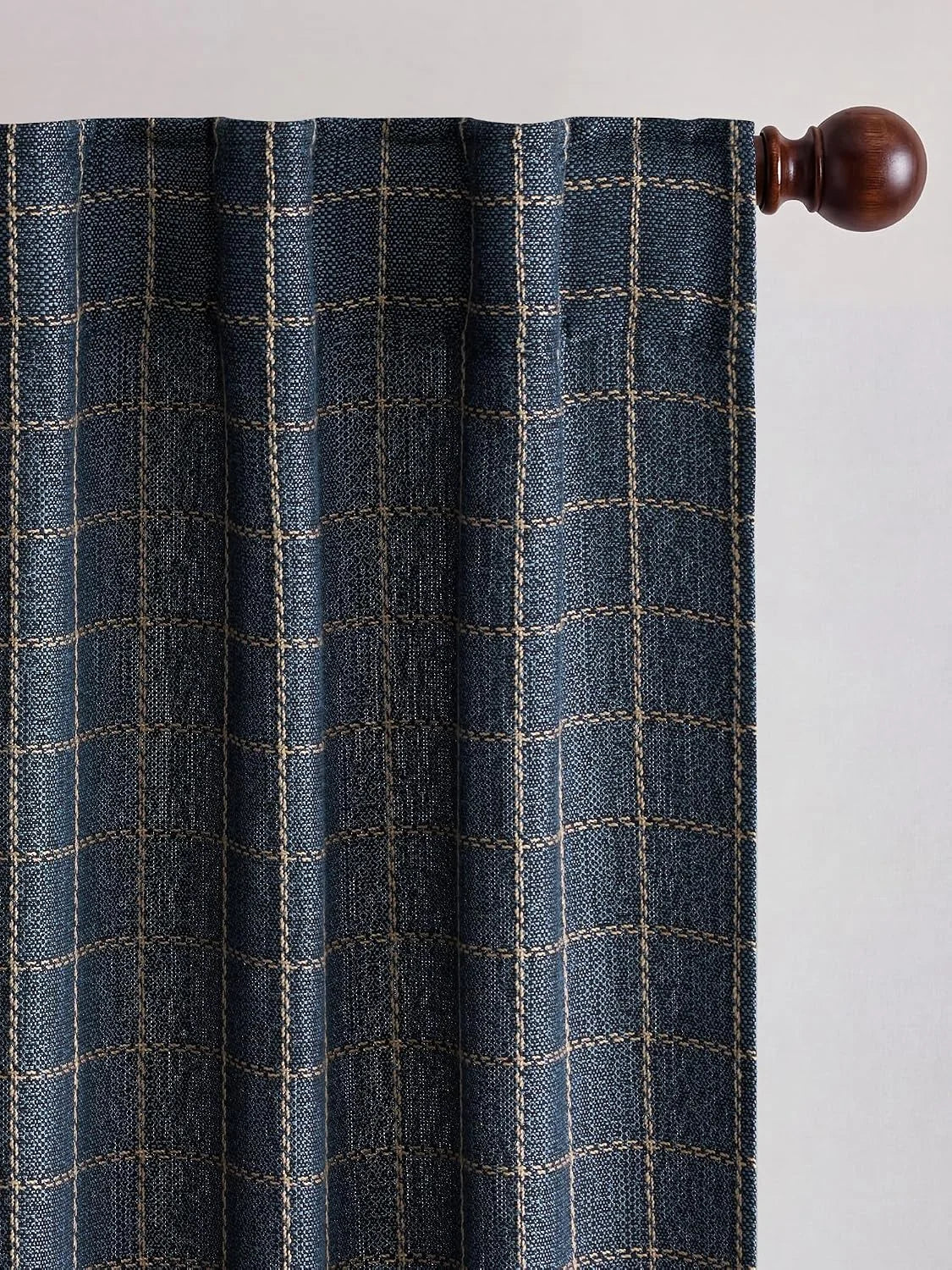 Navy blue woven curtain panel with a light brown grid plaid pattern, hanging on a dark wood rod with finial.