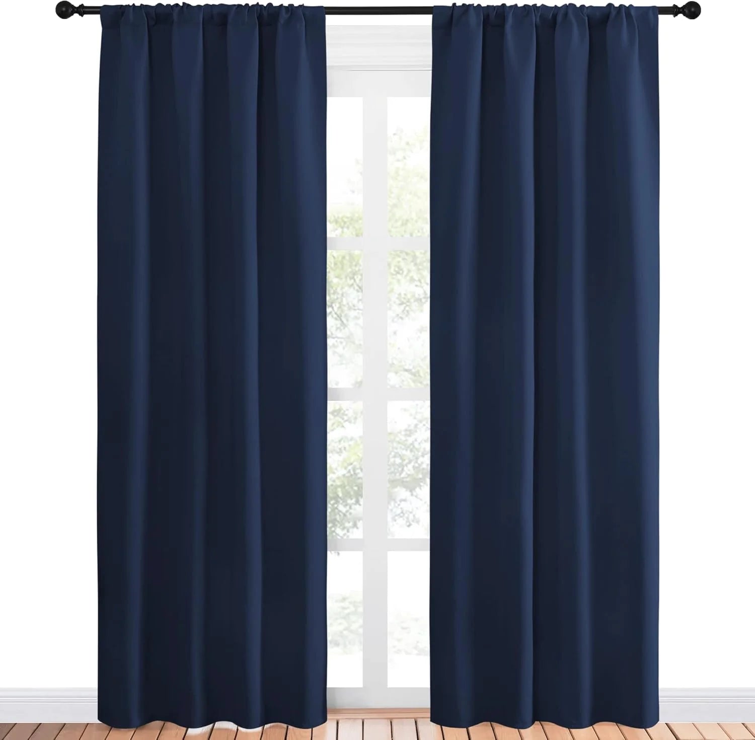 Pair of navy blue rod pocket blackout curtains on black rod in front of bright window, wooden floor.