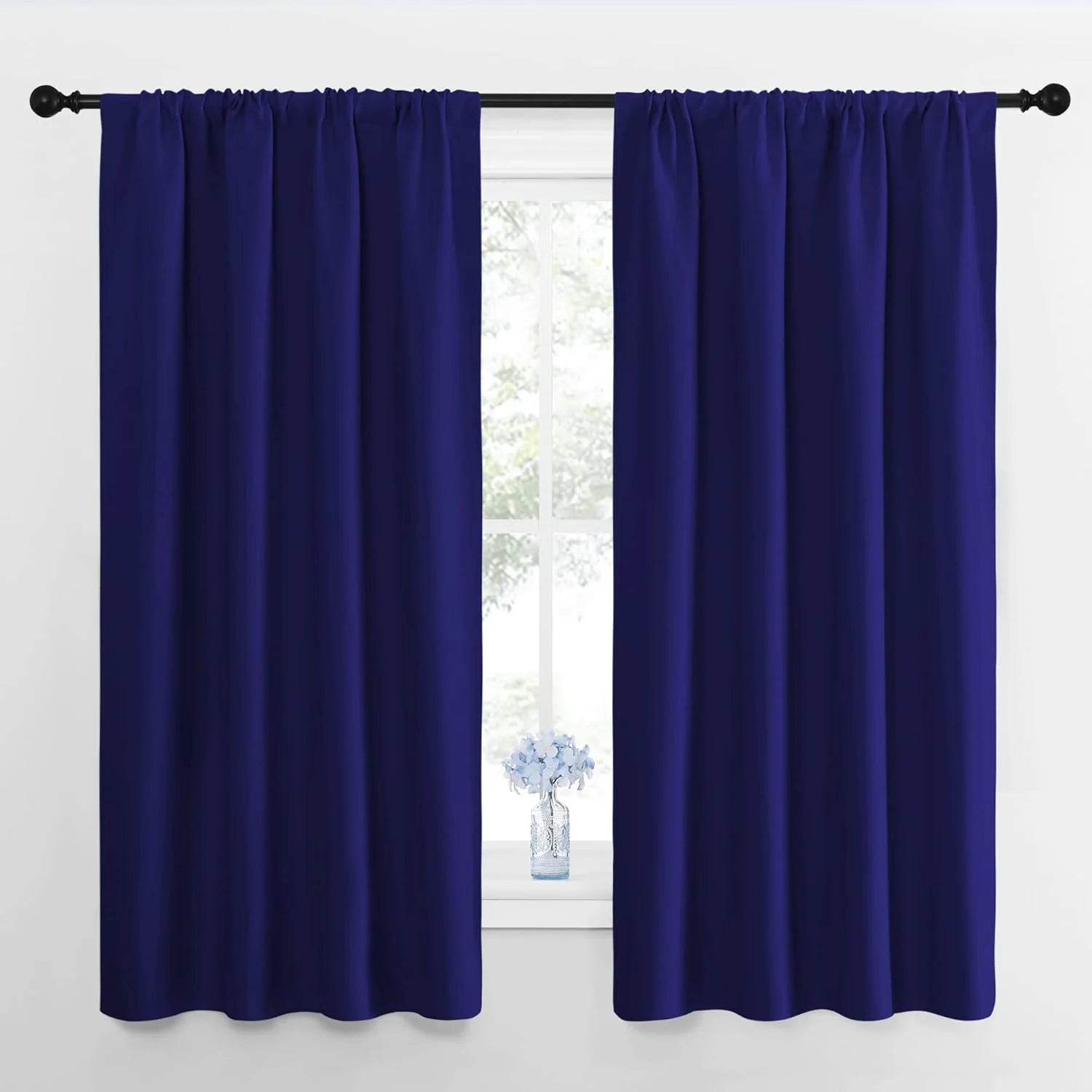 Pair of deep navy blue rod pocket curtains on a black rod over a bright window with white trim.