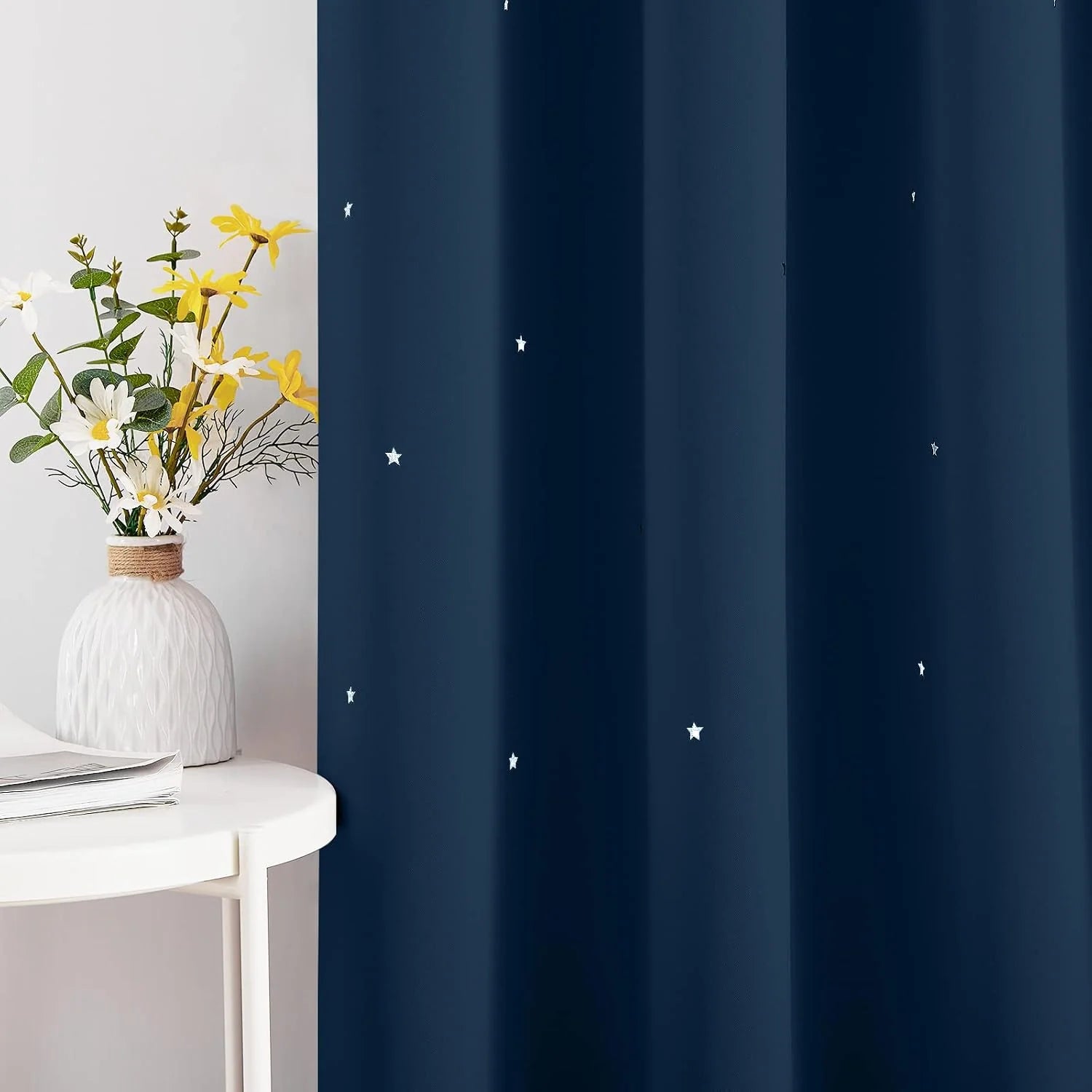 Navy blackout curtain with small white star print beside a white side table and vase