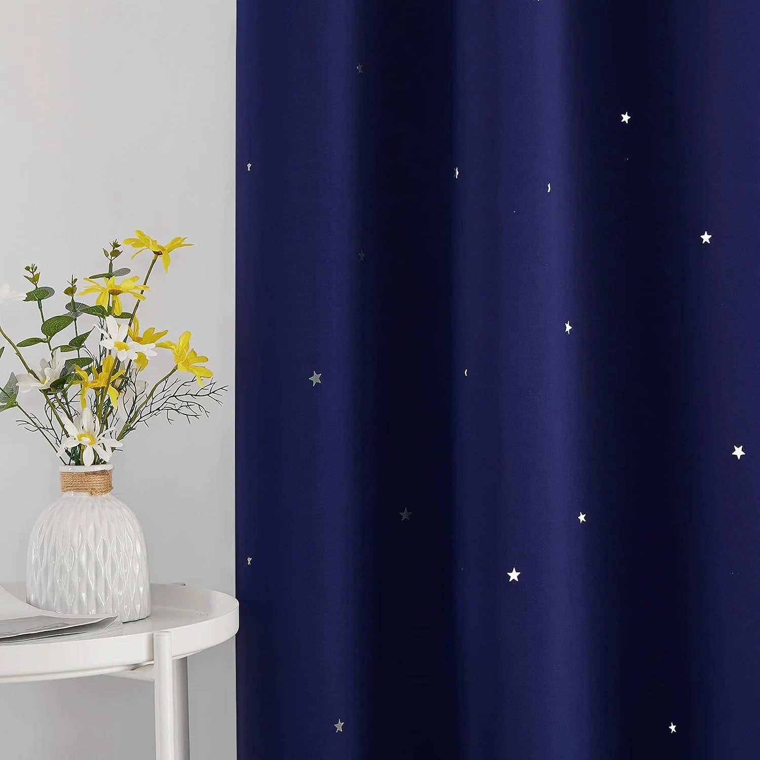 Navy blackout curtain with scattered white star print beside a white table and vase