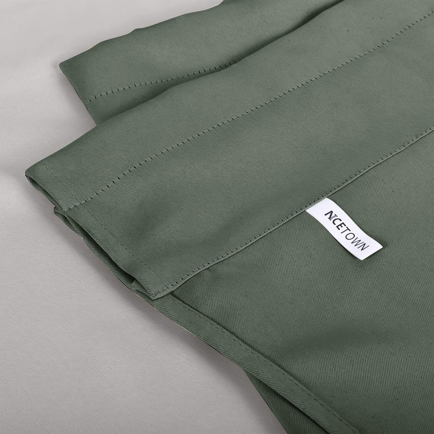 Close-up of NCETOWN sage green woven curtain fabric, showing its subtle twill texture and brand label.