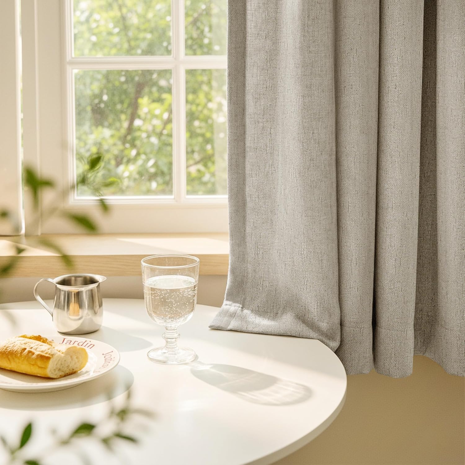 Textured oatmeal fabric room darkening curtains with soft pleats, hanging by a sunny window.