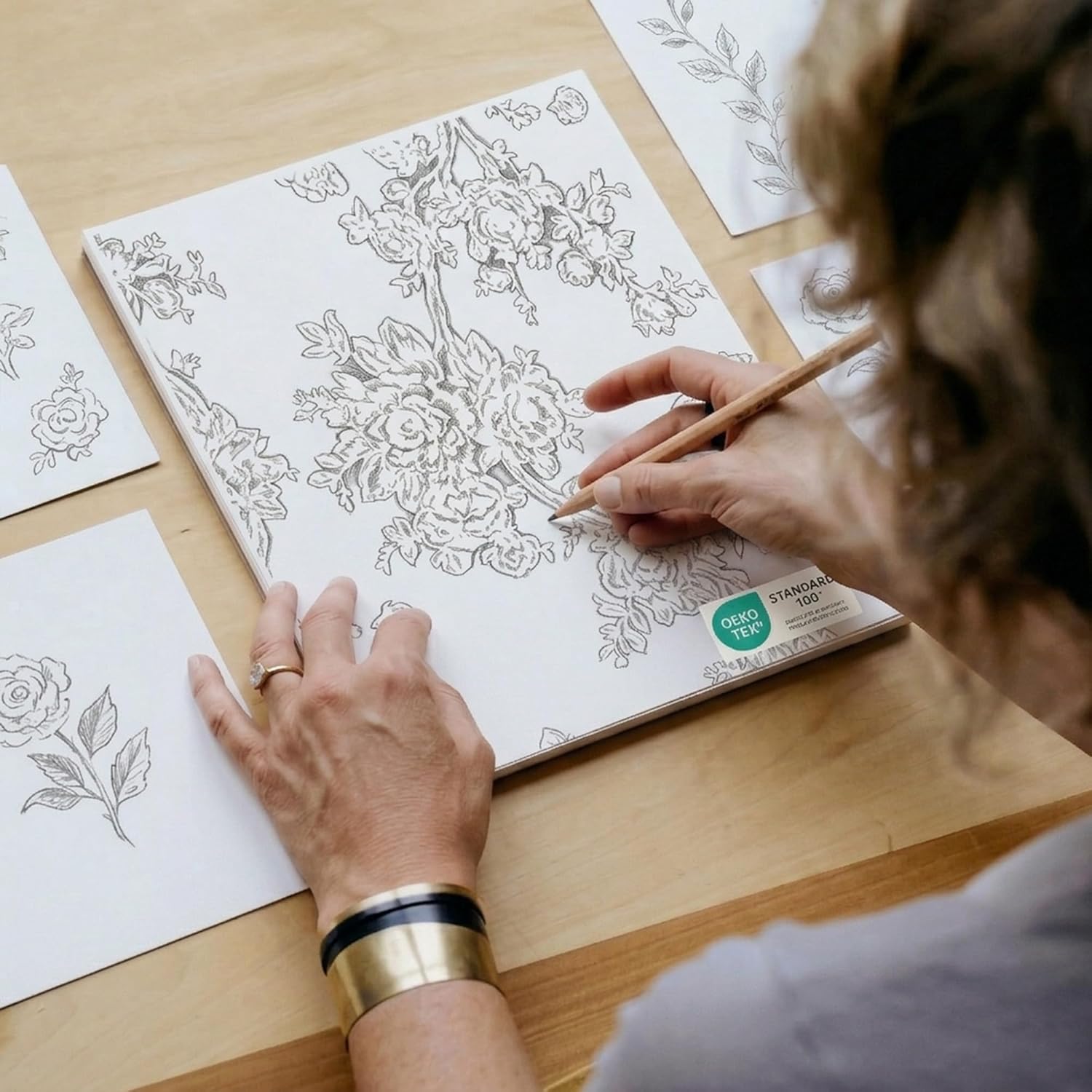 Close-up of artist drawing intricate botanical floral pattern on white OEKO-TEX certified textile fabric.