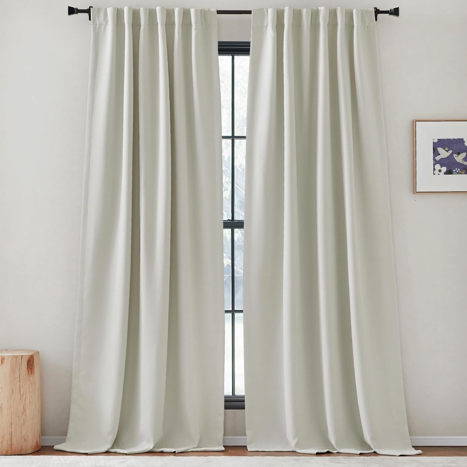 Off-white full-length curtains with a pleated back tab header on a black rod over a window.