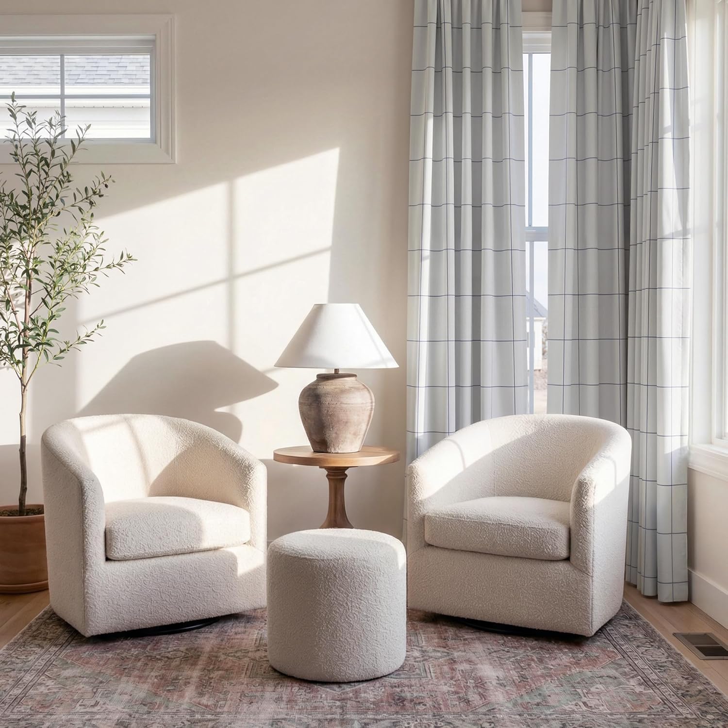Cozy off-white boucle swivel barrel chairs and matching ottoman on a patterned rug.
