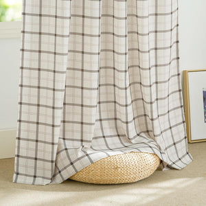 Textured off-white window curtain with brown plaid pattern, pooling on a woven pouf by the window.