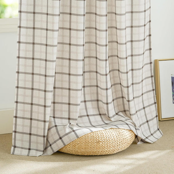 Textured off-white window curtain with brown plaid pattern, pooling on a woven pouf by the window.
