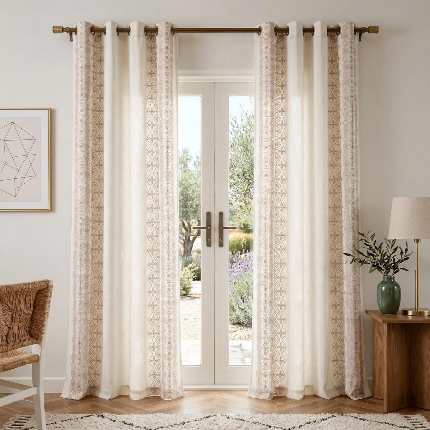 Off-white linen-look curtains with tan geometric embroidered borders and bronze grommets.