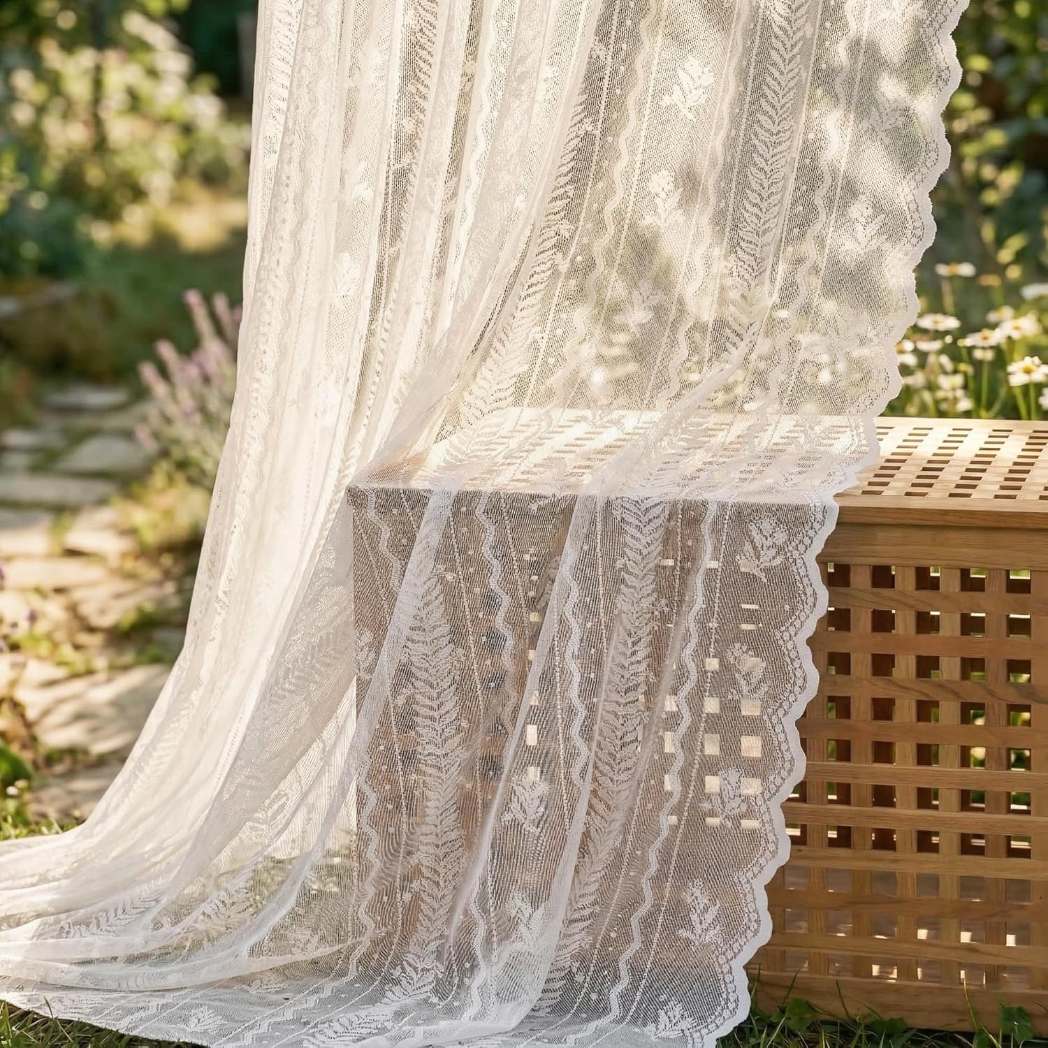 Sheer off-white lace curtain with fern and floral patterns, scalloped edge, draped in a sunny garden.