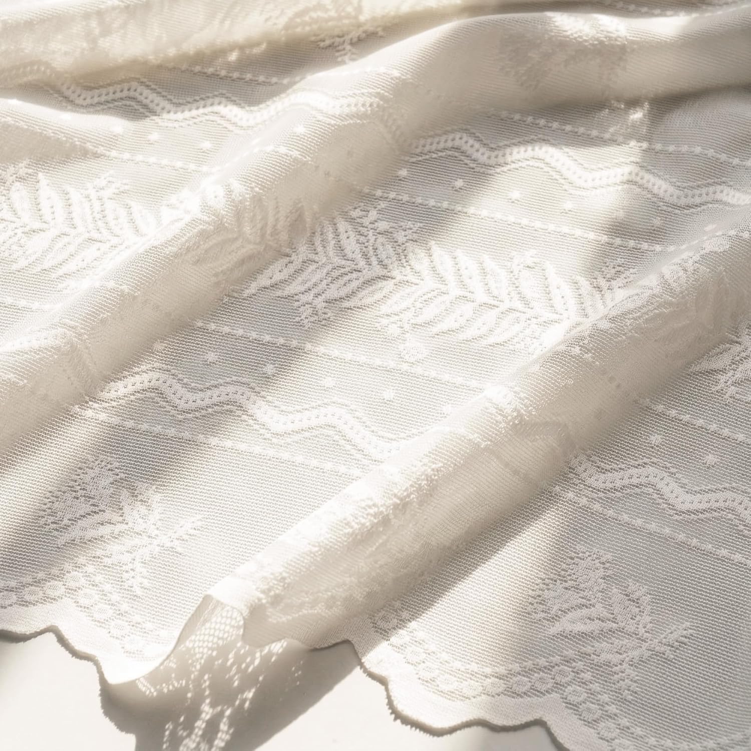Off-white sheer lace fabric with delicate floral and geometric patterns, showing a scalloped edge.
