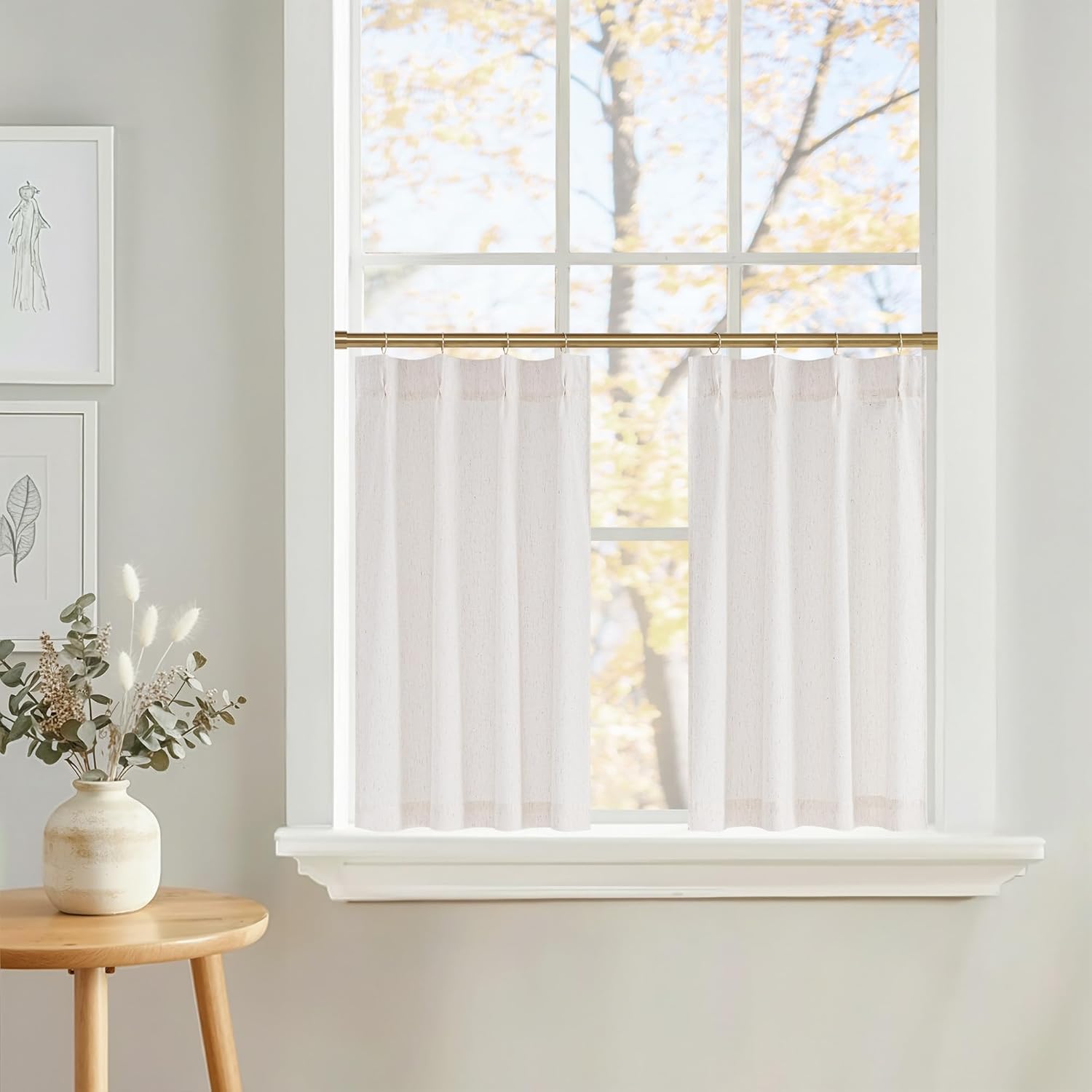 Textured off-white linen blend cafe curtains with back tabs on a brass rod, filtering sunlight.